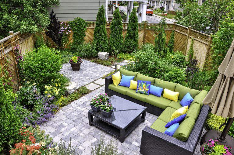 A beautiful small, urban backyard garden featuring a tumbled paver patio, flagstone stepping stones, and a variety of trees, shrubs and perennials add colour and year round interest.